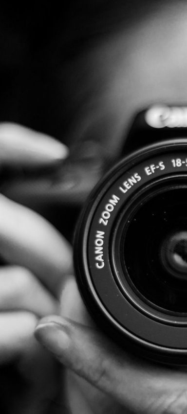 Nahaufnahme einer Hand, die eine Kamera hält, im Fokus auf das Objektiv.