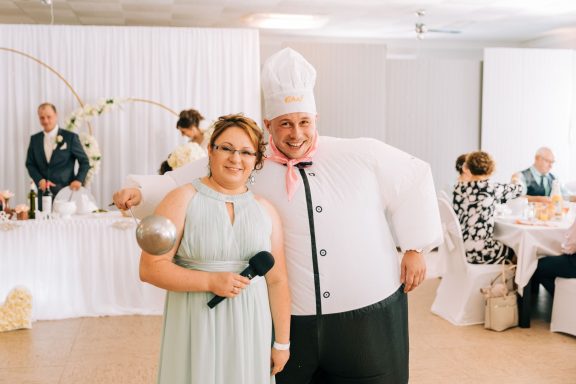 Eine Frau mit Mikrofon und ein Koch in einem festlichen Saal bei einer Feier.