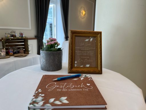 Brauner Gästebuch mit Blumenmotiv und gerahmtem Text auf einem Tisch, daneben ein Stift.
