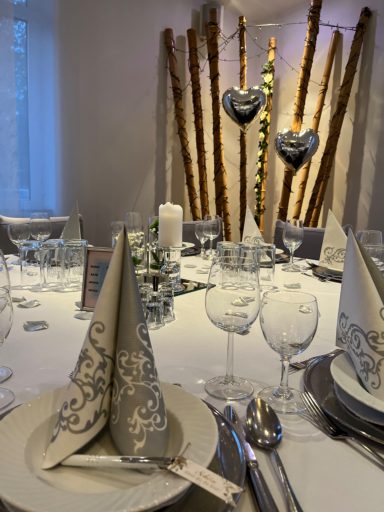 Festlich gedeckter Tisch mit elegantem Geschirr und dekorativen Herzen im Hintergrund.