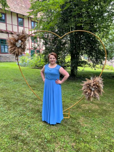 Frau in einem blauen Kleid steht vor einem herzförmigen Rahmen mit Dekorationen.