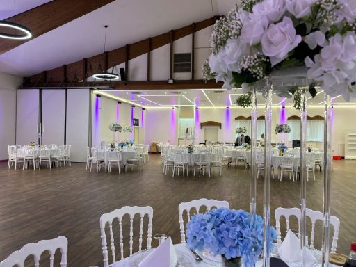 Eleganter Veranstaltungsraum mit weißen Tischen, Blumenarrangements und farbiger Beleuchtung.