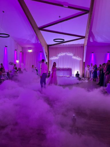 Brautpaar in einem festlich dekorierten Raum mit Nebel und lila Beleuchtung.