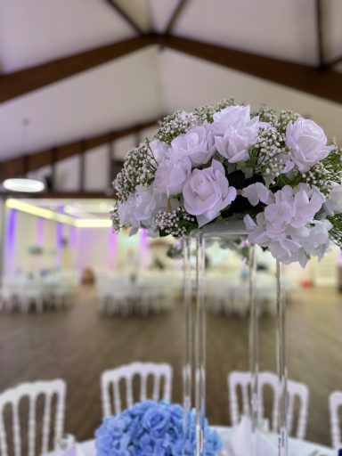 Blumenarrangement in einem eleganten Saal mit Tischen und Stühlen.