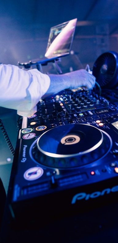 DJ-Mischpult mit Plattenspieler und Laptop, beleuchtet von bunten Lichtern.