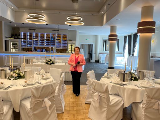 Elegant Restaurant mit gedeckten Tischen und Gastgeberin in rosa Jacke.