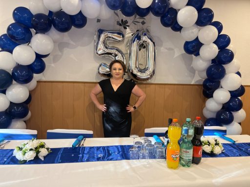 Frau in schwarzem Kleid steht an festlich gedecktem Tisch zum 50. Geburtstag.