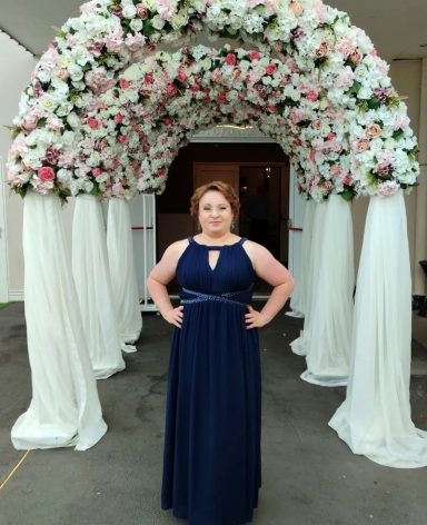 Frau in dunkelblauem Kleid steht unter einem Blumengestell mit weißen Stoffbahnen.