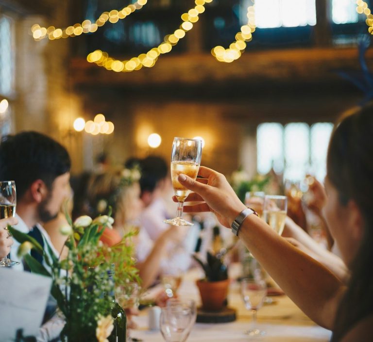 Geselliges Festessen mit Gästen, die Gläser zum Anstoßen heben, umgeben von Blumen.